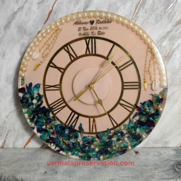 Pink & Blue Theme Resin Varmala Preserved Wall Clock with Roman Numerals, Couple Name, Hashtag, and Wedding Date Immortalized in Epoxy. Half Pearls & Half Floral Decor Adorn This 12-Inch Clock, a Unique Keepsake Preserving the Varmala Moment