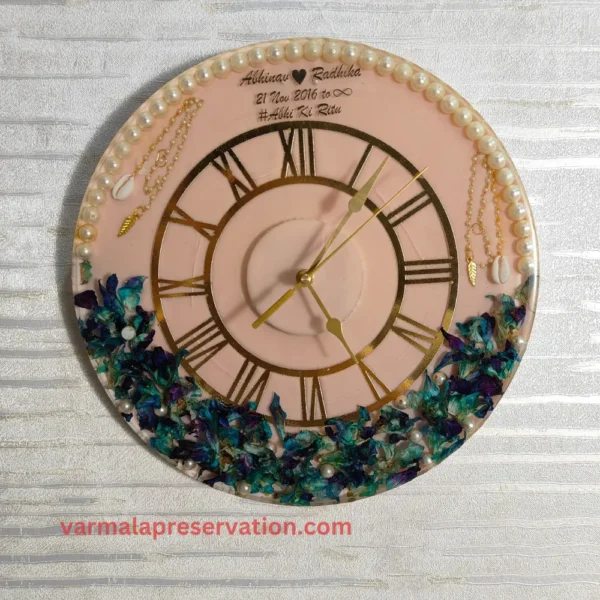 Resin Wall Clock in Pink & Blue Theme with Preserved Varmala, Roman Numerals, Couple Name, Hashtag, and Wedding Date Embedded in Epoxy. Features Half Pearls & Half Floral Decor, Measures 12 Inches
