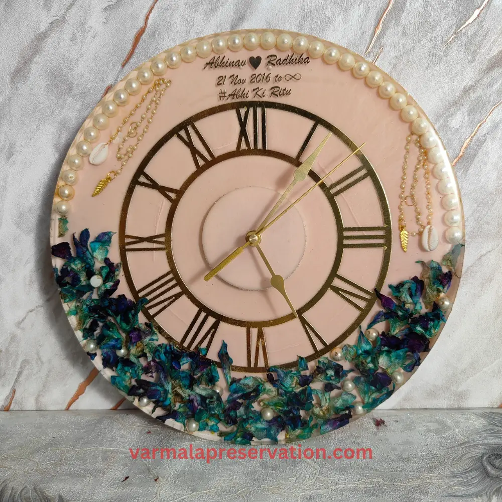 Pink & Blue Theme Resin Varmala Preserved Wall Clock with Roman Numerals, Couple Name, Hashtag, and Wedding Date Immortalized in Epoxy. Half Pearls & Half Floral Decor Adorn This 12-Inch Clock, a Unique Keepsake Preserving the Varmala Moment